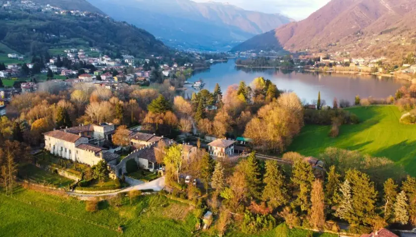 Un antico borgo si affaccia sul lago di Endine, circondato da colline verdi e montagne.