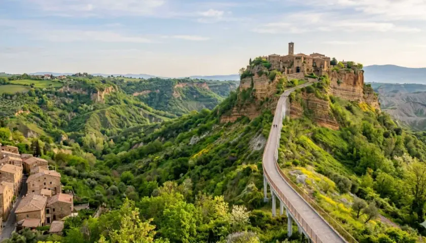 Ponte pedonale verso Civita di Bagnoregio, un borgo medievale arroccato su una rupe, circondato da verdi calanchi.