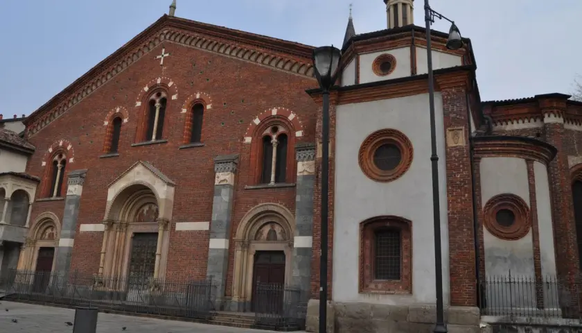 Facciata in mattoni rossi e parte in intonaco bianco della Basilica di Sant'Eustorgio a Milano, con portali decorati e finestre ad arco.