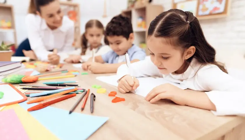 Bambini concentrati scrivono, un'insegnante li osserva. Un'immagine che ispira per una domanda motivazionale TFA sostegno.