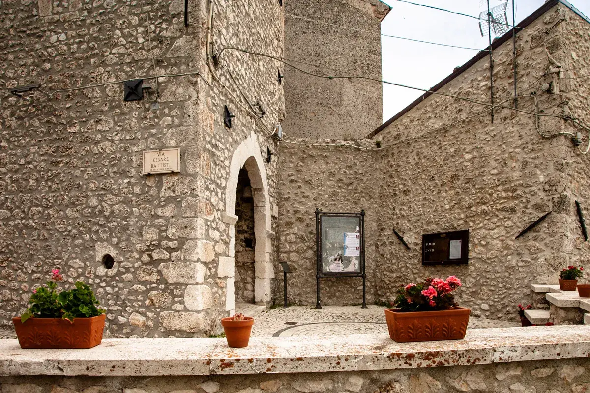 Un angolo suggestivo di Castel del Monte, Abruzzo, con muri in pietra grezza, un arco antico e vasi fioriti che aggiungono colore.