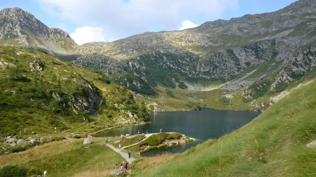 Sentiero panoramico per il giro dei 5 laghi a Madonna di Campiglio, con escursionisti che ammirano il lago alpino e le montagne circostanti.