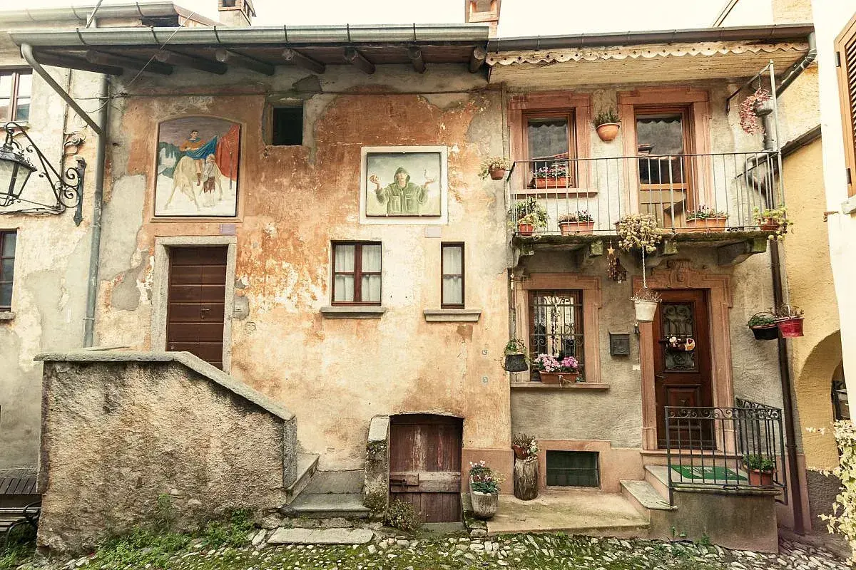 Antica facciata con affreschi e balcone fiorito. Un invito a scoprire cosa vedere ad Arcumeggia, tra arte e storia.