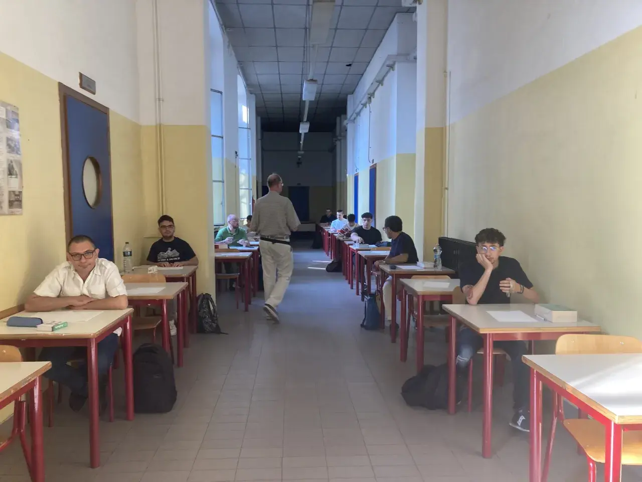 Studenti seduti ai banchi in un'aula scolastica, concentrati sull'esame di quinta elementare. Un insegnante cammina tra i banchi.
