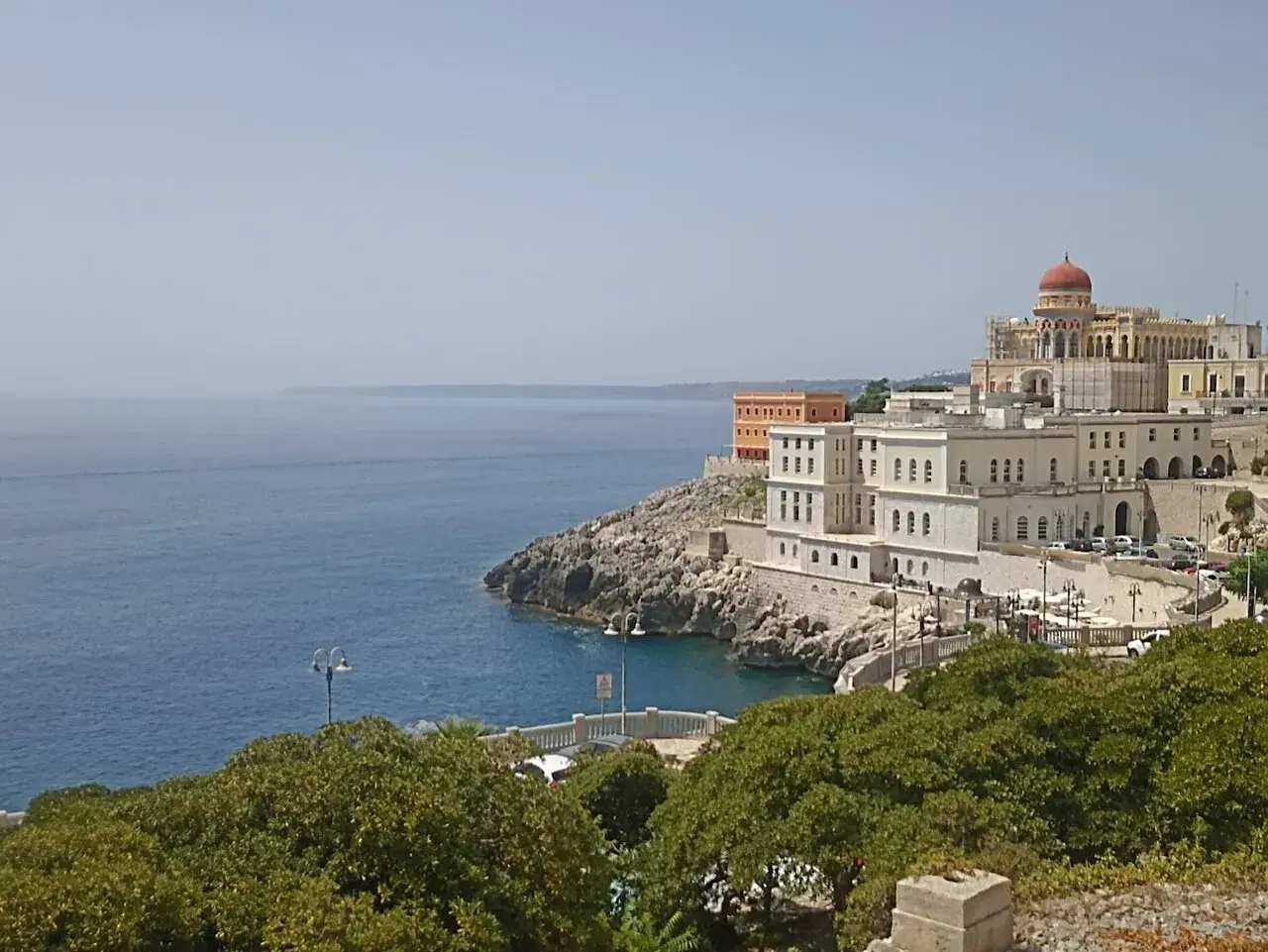 Vista sul mare e sul complesso dell'istituto alberghiero Santa Cesarea Terme, con edifici bianchi e una cupola rossa.