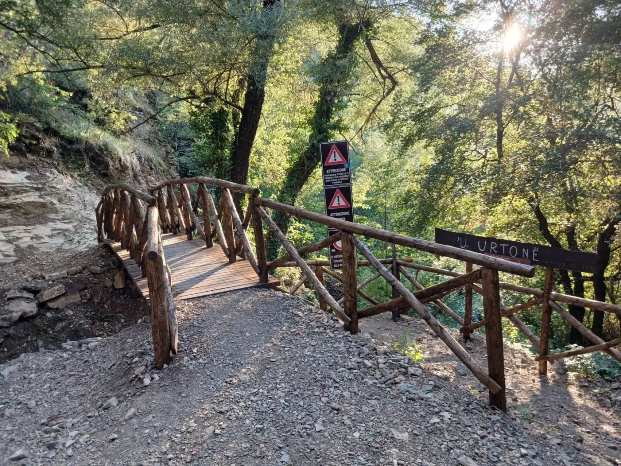 Ponte in legno rustico conduce verso le cascate di San Fele, immerso nel verde e illuminato dal sole.