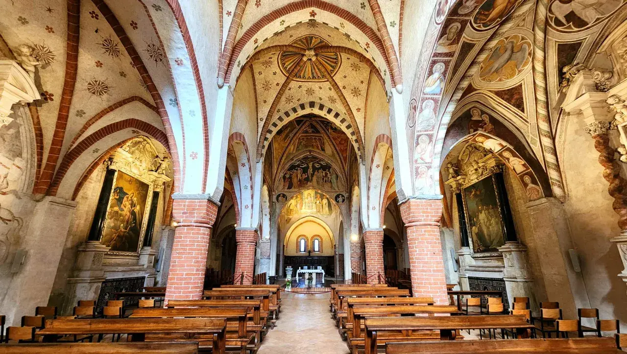Interno dell'abbazia di Viboldone con volte affrescate, colonne in mattoni e panche di legno.