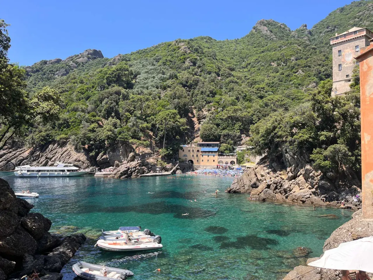 Baia di San Fruttuoso con acque cristalline, barche e persone che nuotano. Un luogo ideale per il trekking e il relax.