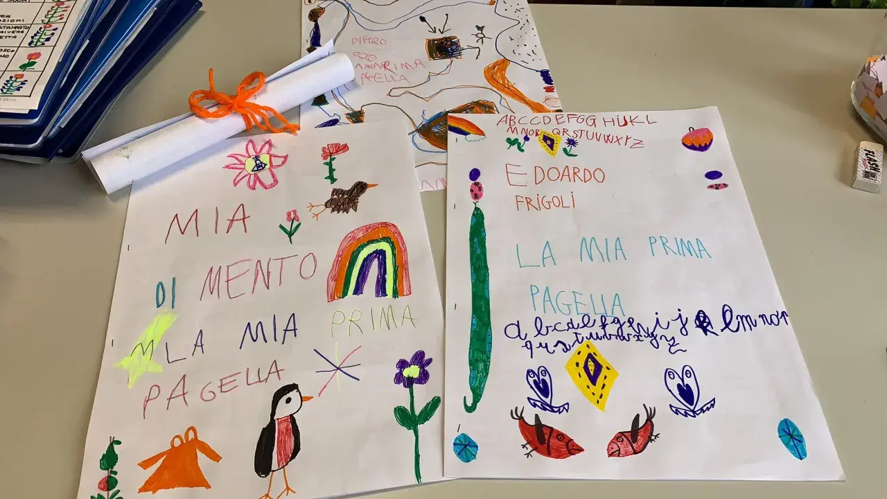 Disegni e scritte a mano, tra cui "Mia Pagella" e l'alfabeto, mostrano i voti elementari di bambini.