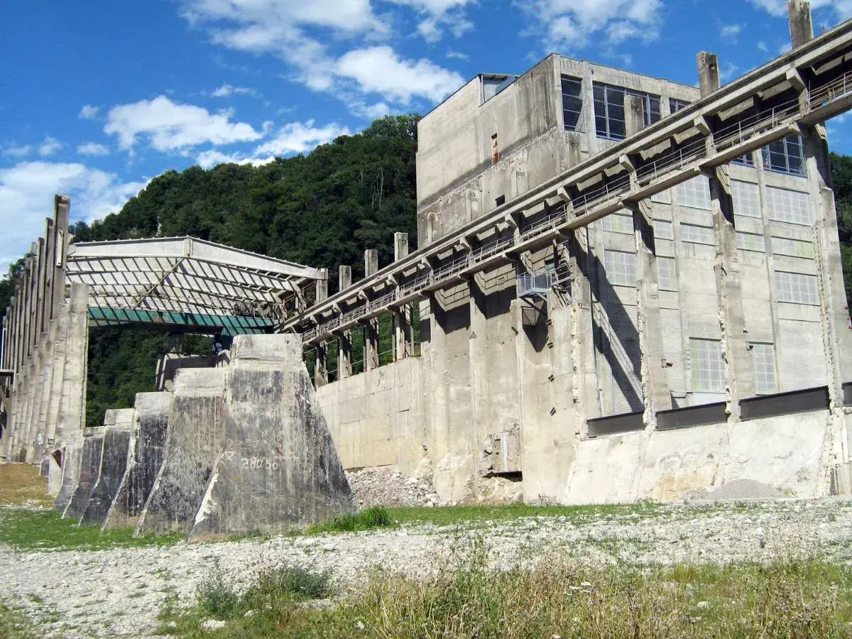 Imponente struttura industriale abbandonata nel parco delle gole della Breggia, con passerelle e finestre che si stagliano contro il cielo azzurro.