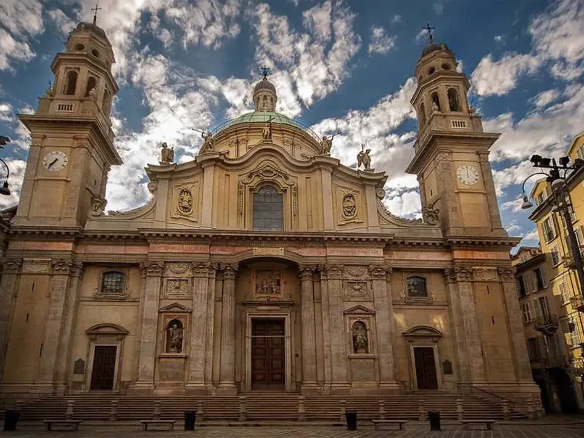 La maestosa facciata della chiesa Sant'Alessandro a Milano, con le sue torri campanarie e la cupola, si staglia contro un cielo azzurro e nuvoloso.