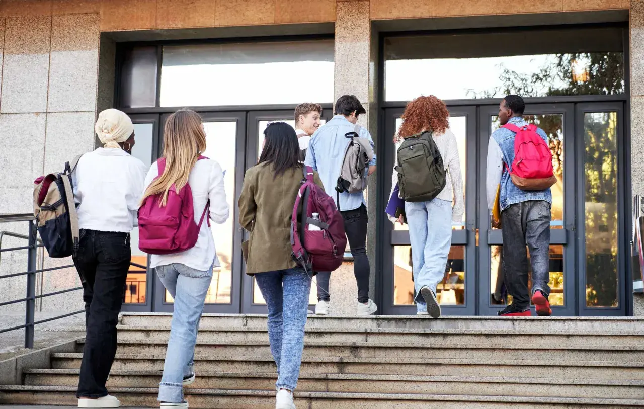 Gruppo di studenti con zaini sale le scale verso l'edificio scolastico, forse per affrontare una grave punizione scolastica.