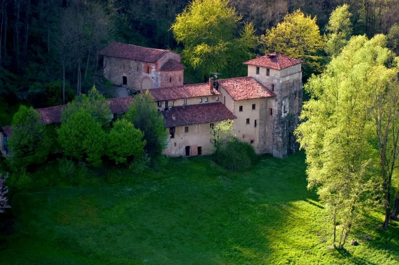 Antico monastero di Torba immerso nel verde, con tetti rossi e torri in pietra, circondato da alberi rigogliosi.