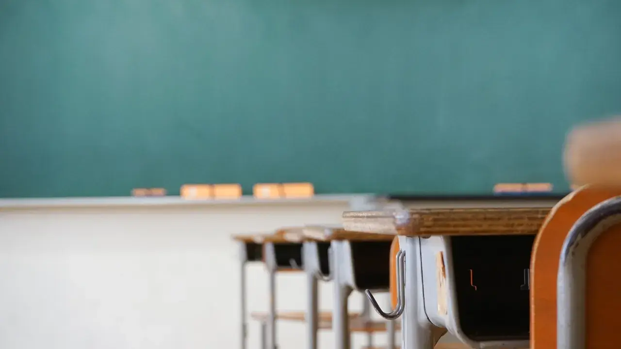 Banchi vuoti in aula, con lavagna verde sullo sfondo. Chissà quanto guadagna un professore delle medie per insegnare qui.