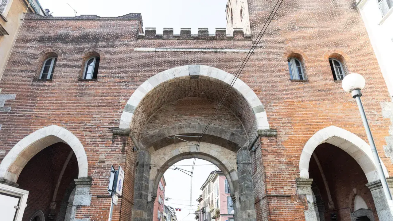 La Porta Ticinese, con i suoi archi in pietra e mattoni rossi, accoglie la vista di una strada milanese.