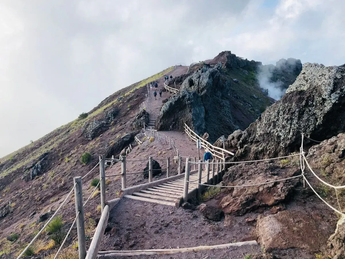 Sentiero sul gran cono Vesuvio, con persone che salgono verso il cratere fumante.
