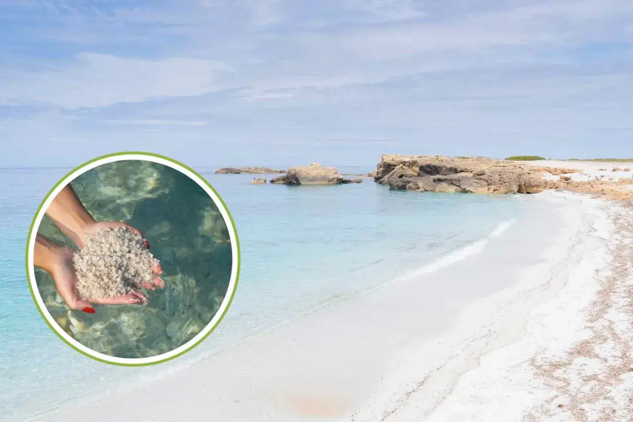 Mani raccolgono sabbia bianca e fine su una spiaggia di vetro in Sardegna, con acque cristalline e rocce sullo sfondo.
