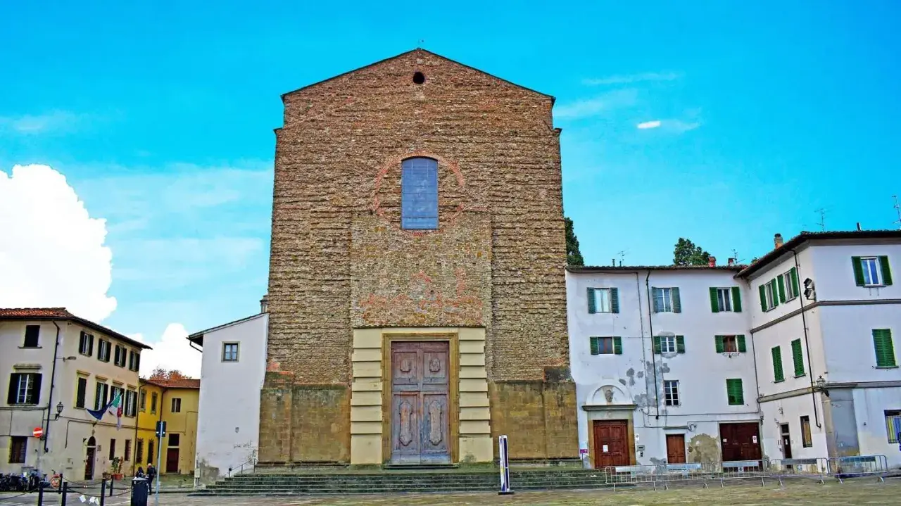 La facciata in pietra grezza di Santa Maria del Carmine domina la piazza, con un grande portale in legno e un rosone blu.