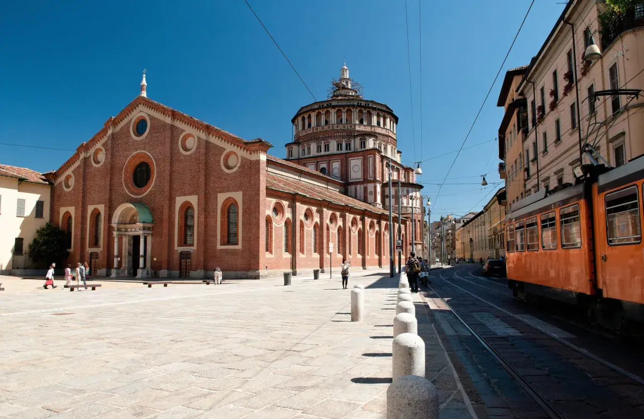 Piazza antistante Santa Maria delle Grazie con tram arancione in transito.