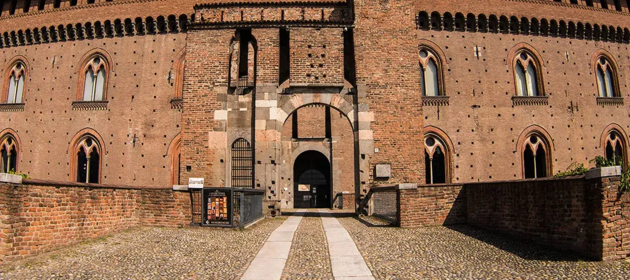 Ingresso principale del castello visconteo di Pavia, con mura in mattoni rossi, finestre ogivali e un ampio portone ad arco.
