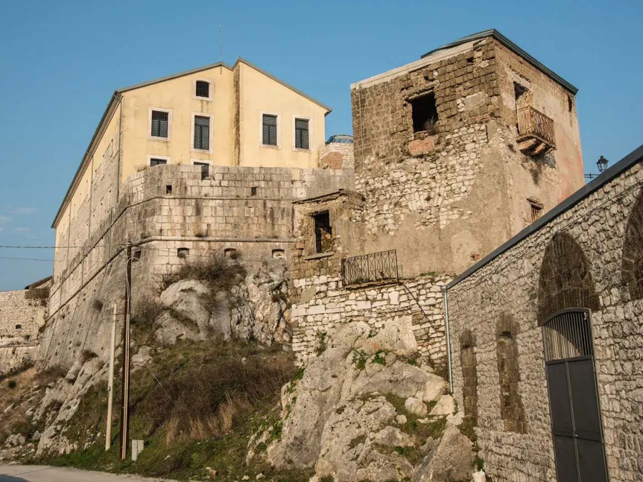 Antiche mura e un edificio giallo a Montesarchio, Benevento, si stagliano contro il cielo azzurro.