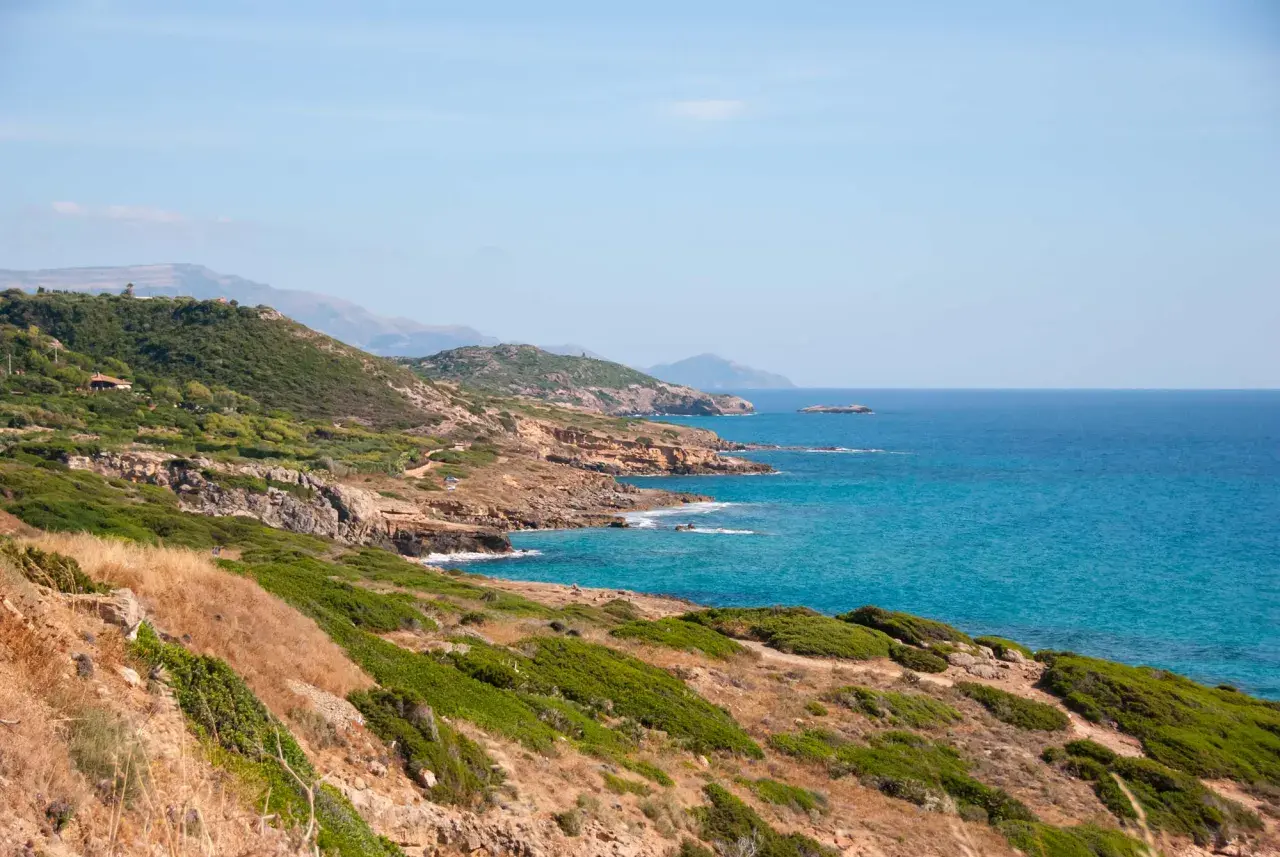 Costa selvaggia tra Alghero e Bosa, con macchia mediterranea, rocce dorate e mare turchese.