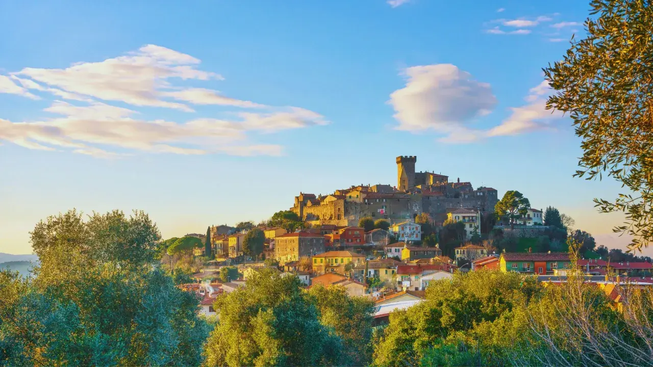 Un caparbio paese arroccato su una collina, con un castello imponente e case colorate, illuminato dalla luce dorata del tramonto.