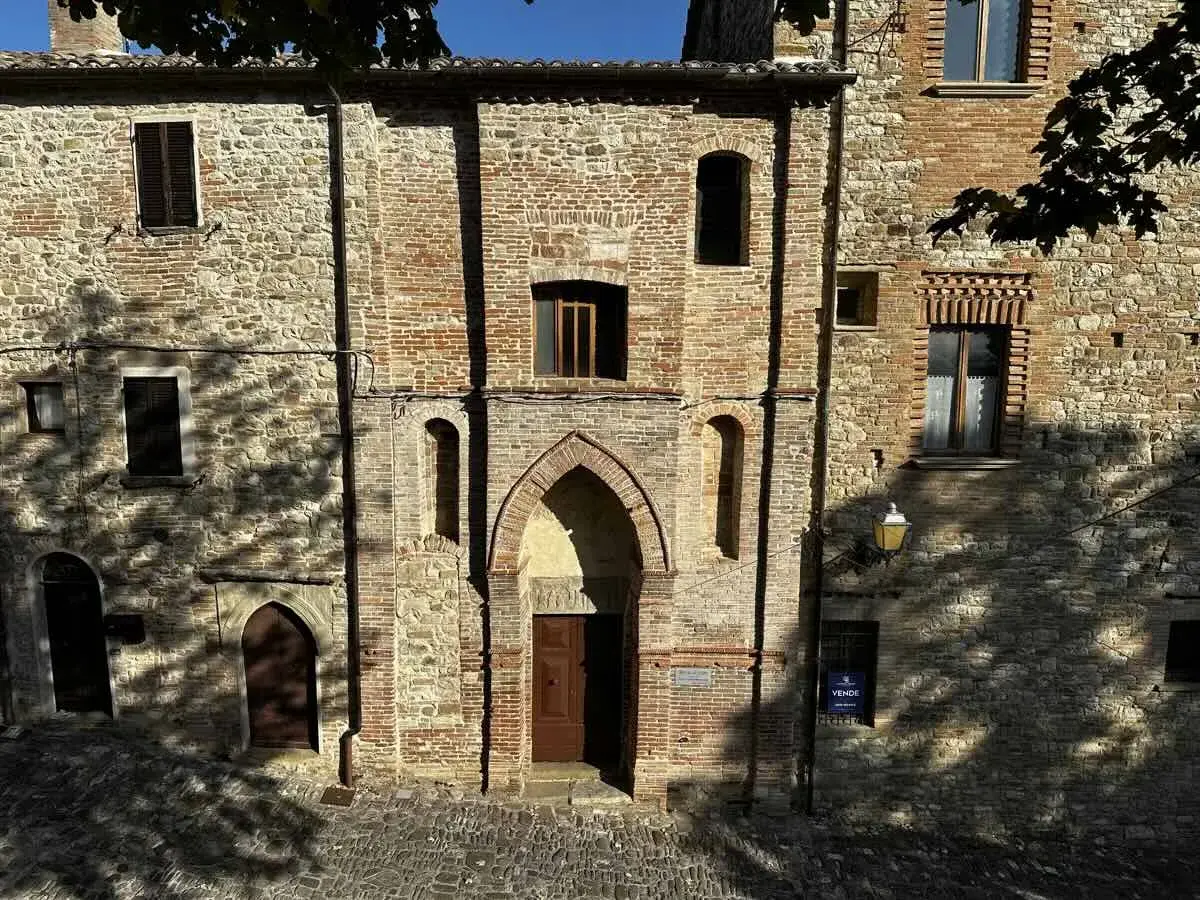 Antica facciata in pietra e mattoni a Macerata Feltria, con un portale ad arco e finestre storiche.