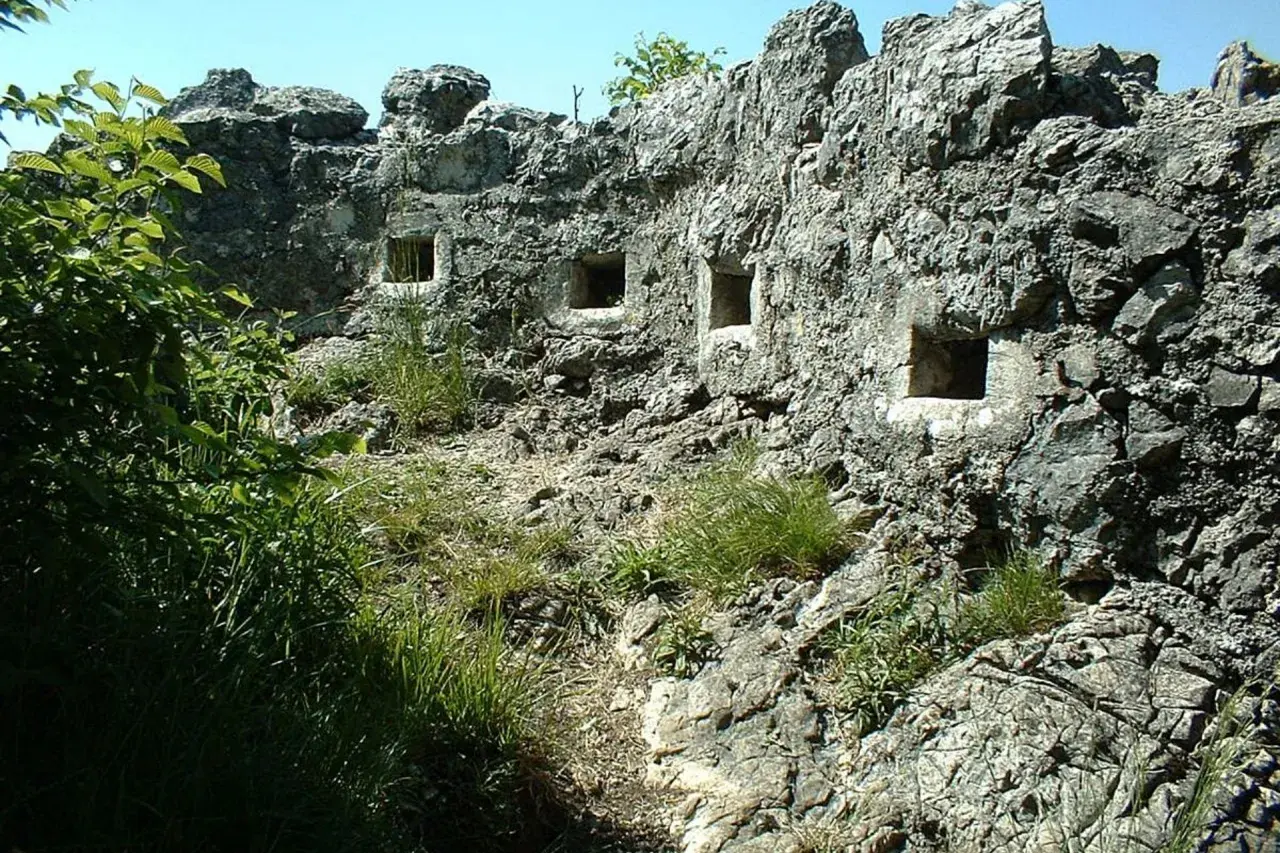 Antiche trincee della Linea Cadorna scavate nella roccia, con feritoie che si affacciano su un paesaggio verdeggiante.