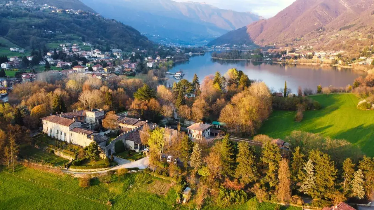 Un antico borgo si affaccia sul lago di Endine, circondato da colline verdi e montagne.