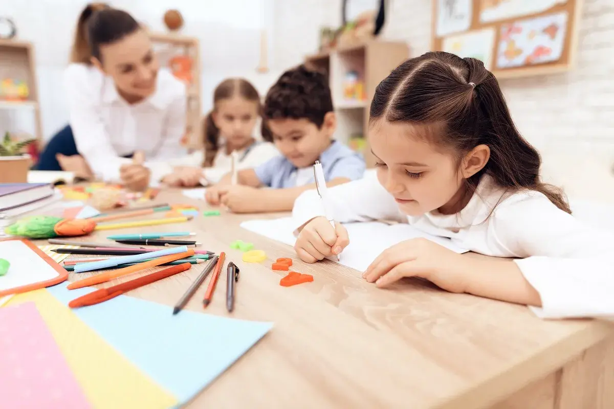 Bambini concentrati scrivono, un'insegnante li osserva. Un'immagine che ispira per una domanda motivazionale TFA sostegno.
