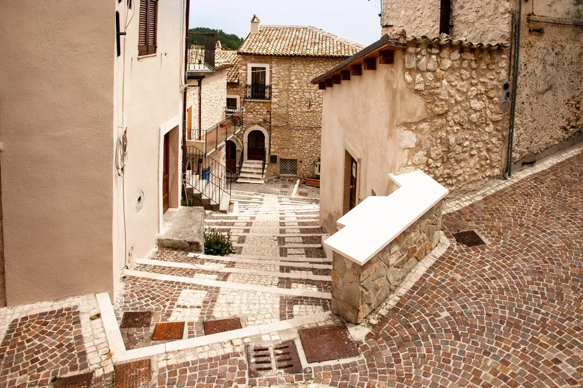 Un vicolo di pietra a Castel del Monte, Abruzzo, con scalinate che salgono tra case antiche e pavimentazioni a mosaico.
