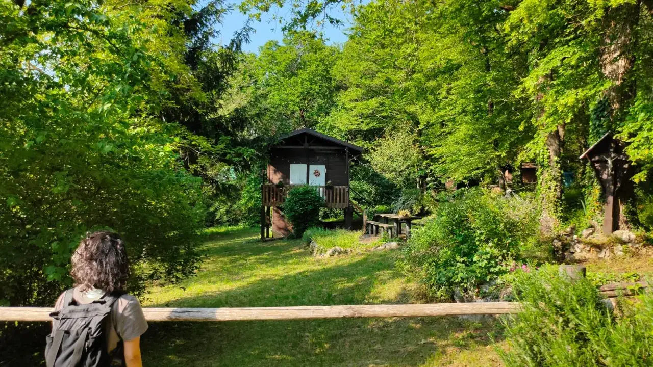 Una persona con zaino osserva una casetta nel bosco, un luogo ideale dove andare in vacanza da soli per immergersi nella natura.