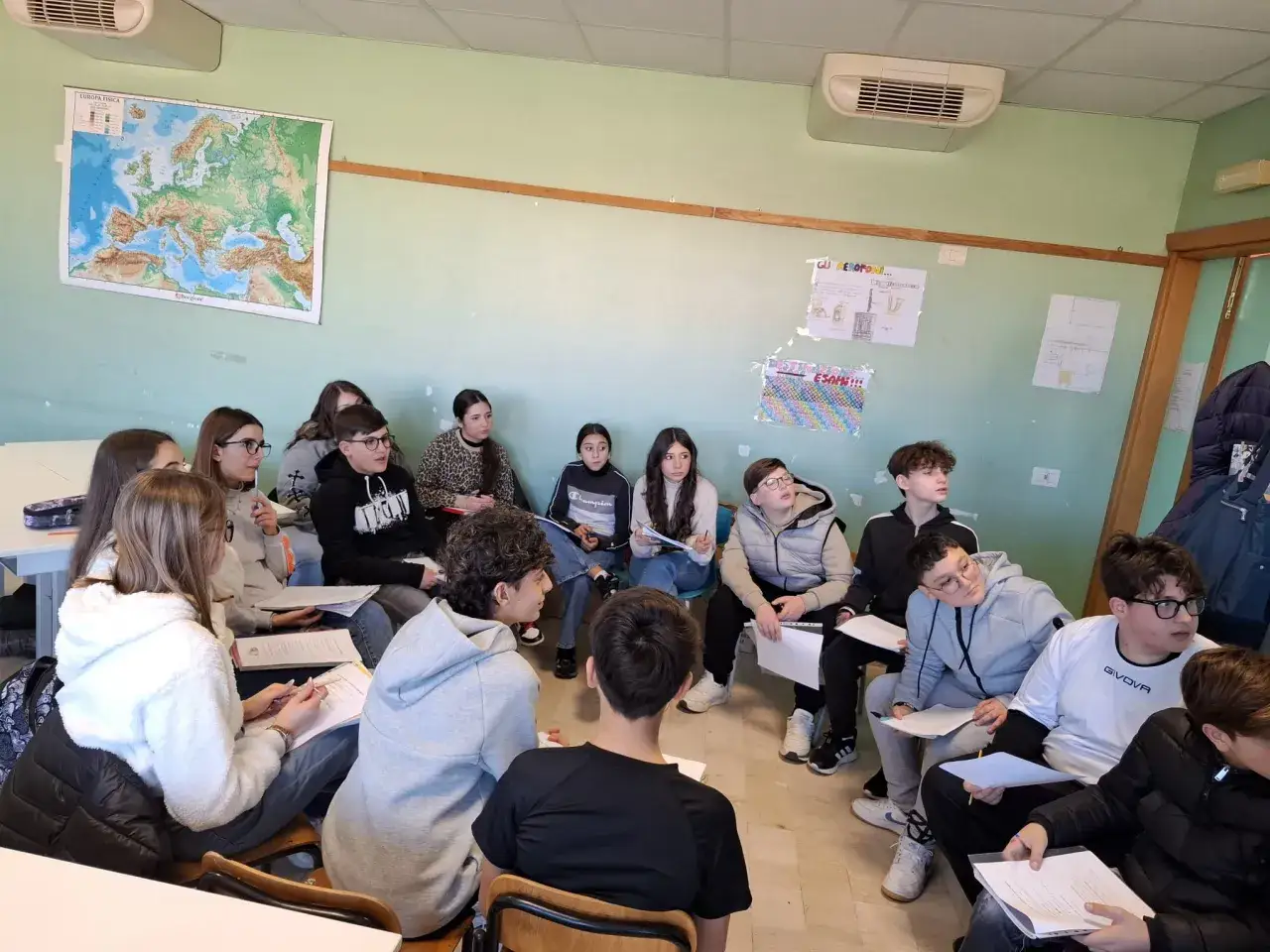 Ragazzi in classe discutono, sviluppando competenze trasversali scuola. Una mappa dell'Europa è appesa al muro.