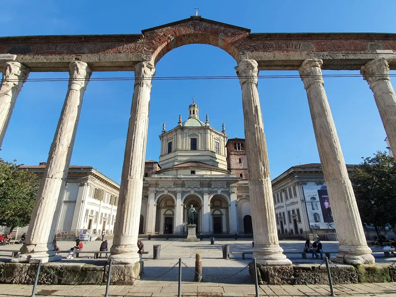 Le imponenti colonne di San Lorenzo incorniciano la Basilica di San Lorenzo Maggiore a Milano, sotto un cielo azzurro.
