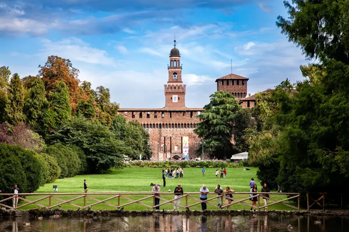 Il maestoso Castello Sforzesco domina il parco, con persone che passeggiano e si rilassano sull'erba verde.