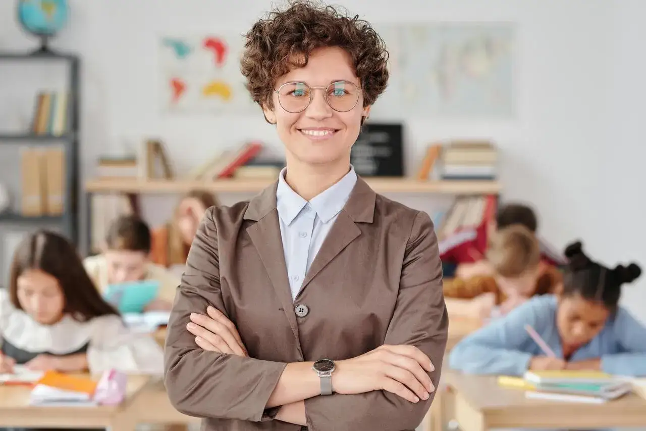 Insegnante sorridente in aula, con studenti che studiano. Il suo look professionale suggerisce che comprende il pdp significato, supportando ogni studente.