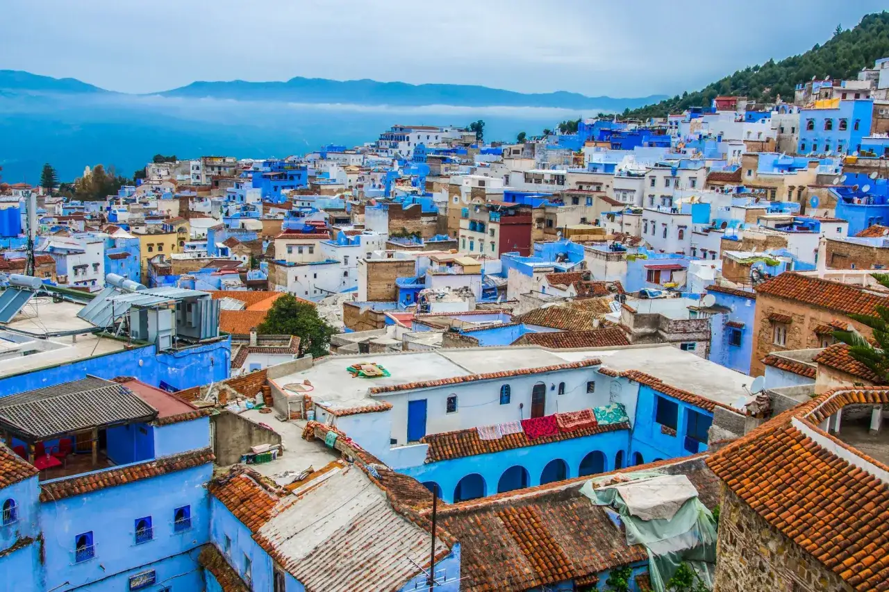 La citt&agrave; azzurra del Marocco, Chefchaouen, si estende su una collina con case dipinte di blu e tetti in terracotta, incorniciata da montagne nebbiose.