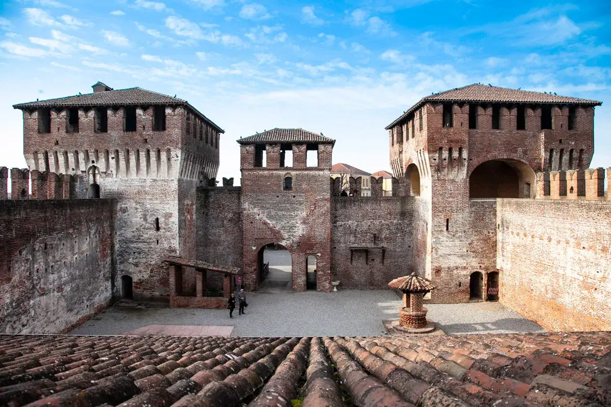 Il castello di Soncino, con le sue imponenti torri in mattoni rossi e le mura merlate, si staglia sotto un cielo azzurro e nuvoloso.