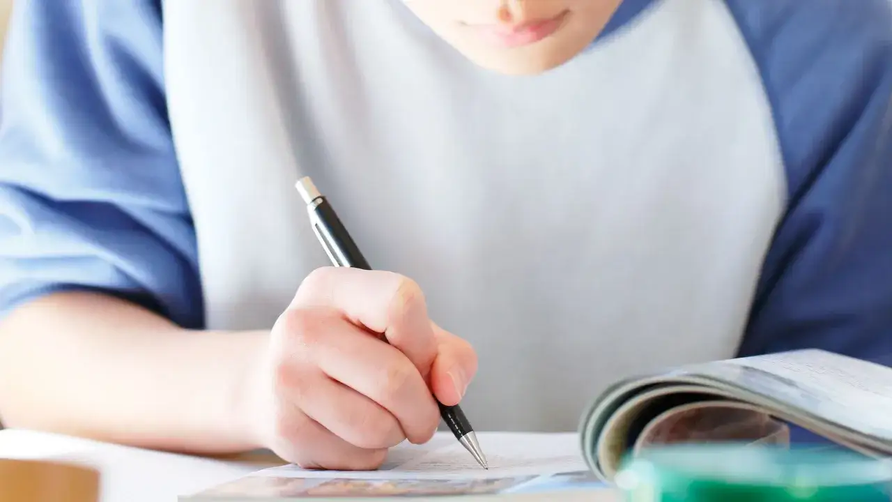 Ragazzo latino alle medie studia con impegno, scrivendo su un quaderno aperto.