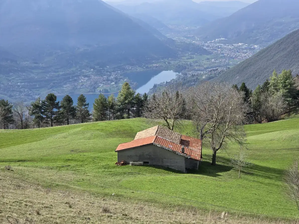 Un casolare con tetto rosso su un prato verde, con vista sul lago di Endine e le montagne nebbiose in lontananza.