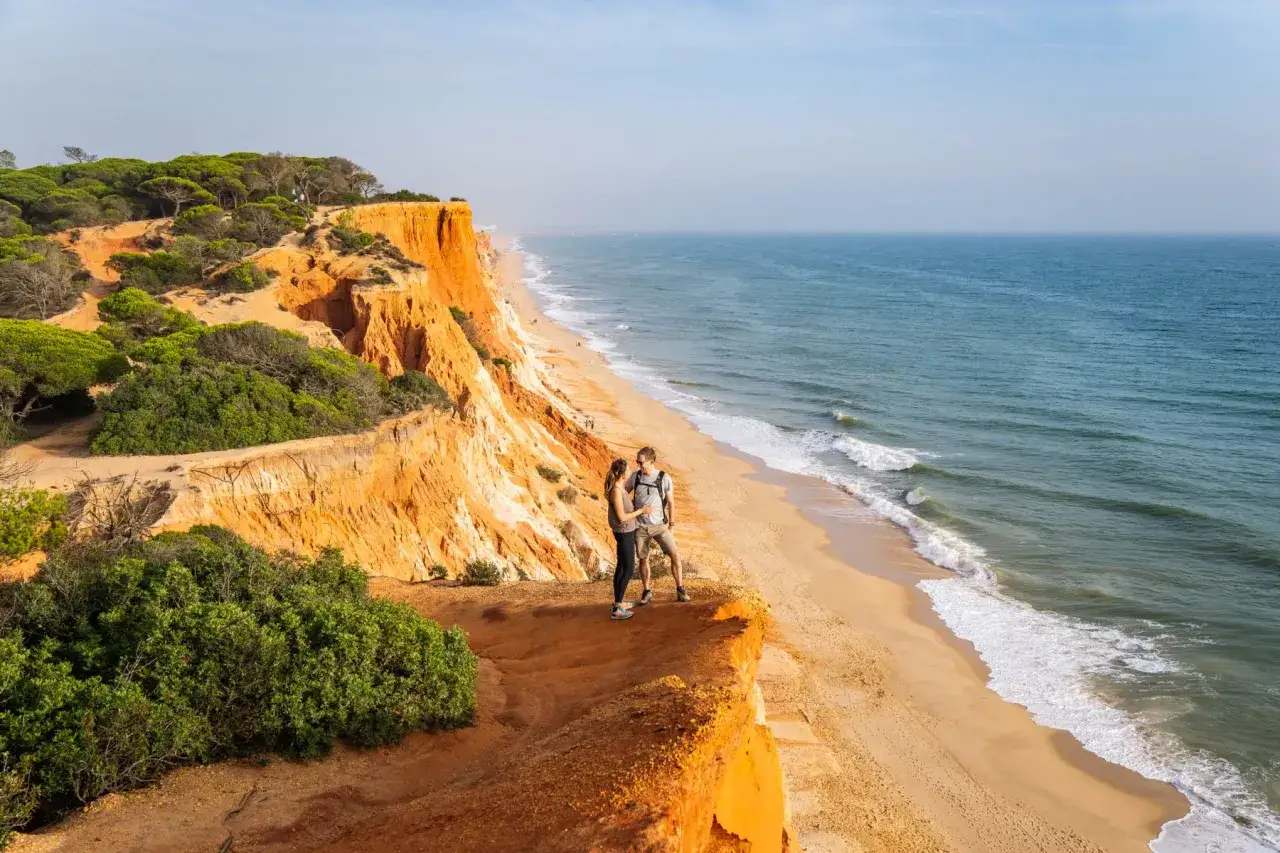Coppia su scogliere arancioni, con vista sul sentiero dei pescatori Portogallo e sull'oceano.