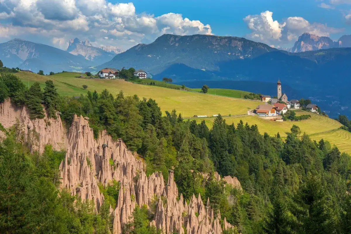 Paesaggio alpino con piramidi di terra e un villaggio. Per raggiungere il trenino del Renon, goditi questa vista mozzafiato.