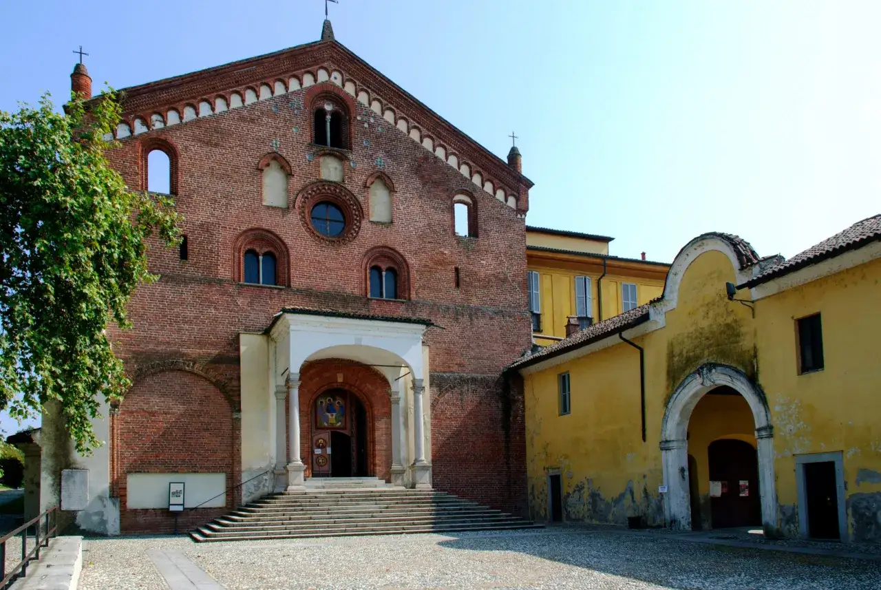 L'imponente facciata in mattoni rossi dell'abbazia di Morimondo si staglia contro il cielo azzurro, con un portico bianco che invita all'ingresso.