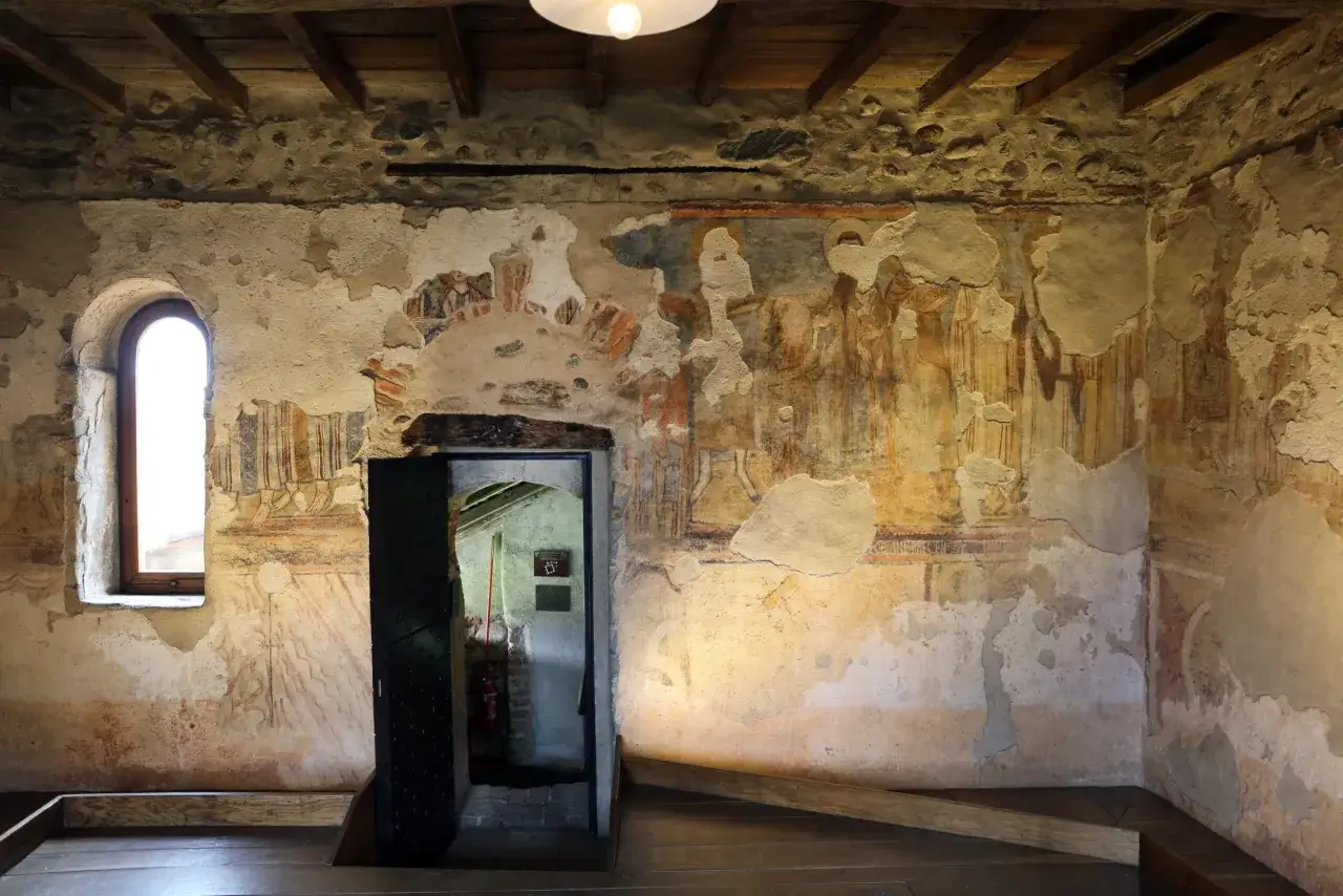 Affreschi sbiaditi di figure sacre adornano le pareti del monastero di Torba, con una finestra ad arco che illumina la scena.