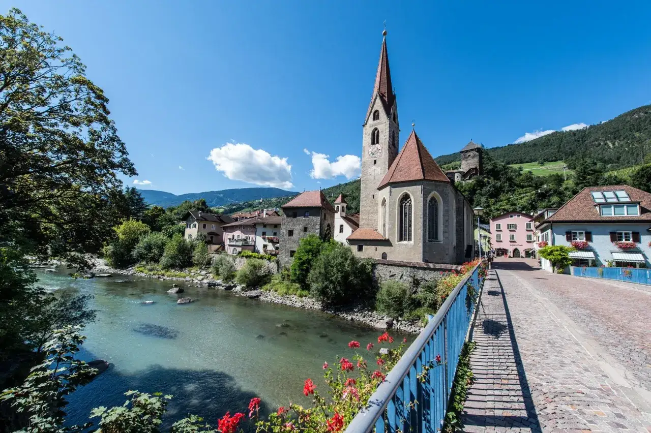Un fiume scorre accanto a un paese alpino con una chiesa imponente. L'altitudine chiusa Bolzano offre panorami mozzafiato.