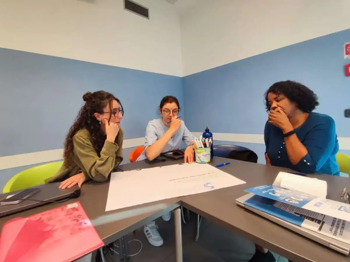 Tre donne discutono attorno a un tavolo, con fogli e materiale didattico. Forse è qui che ho scelto di fare l'insegnante perché amo condividere idee.