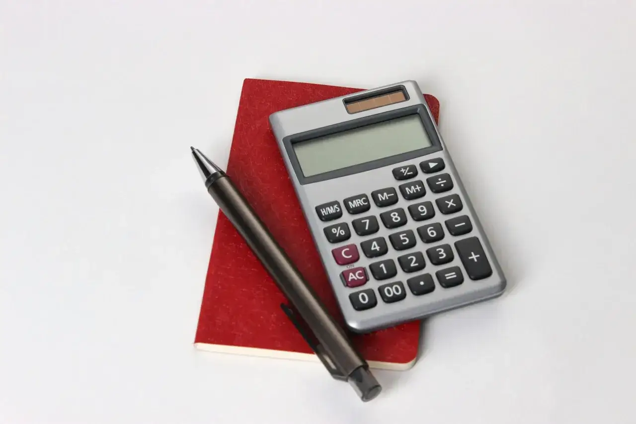 Calcolatrice, penna e taccuino rosso, utili per consultare la tabella importi pensione insegnanti.