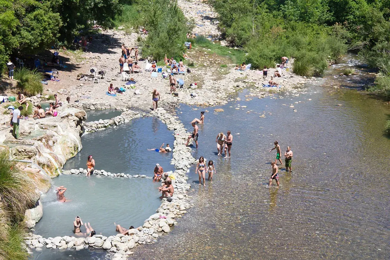 Persone si rilassano nelle san gimignano terme libere, godendosi le acque naturali e il sole in un paesaggio verdeggiante.