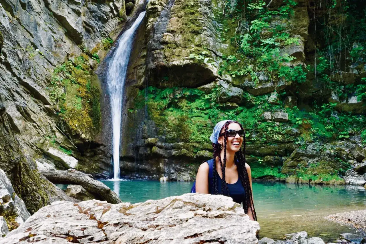 Una ragazza sorride felice davanti alle cascate di San Fele, immersa nella natura rigogliosa.